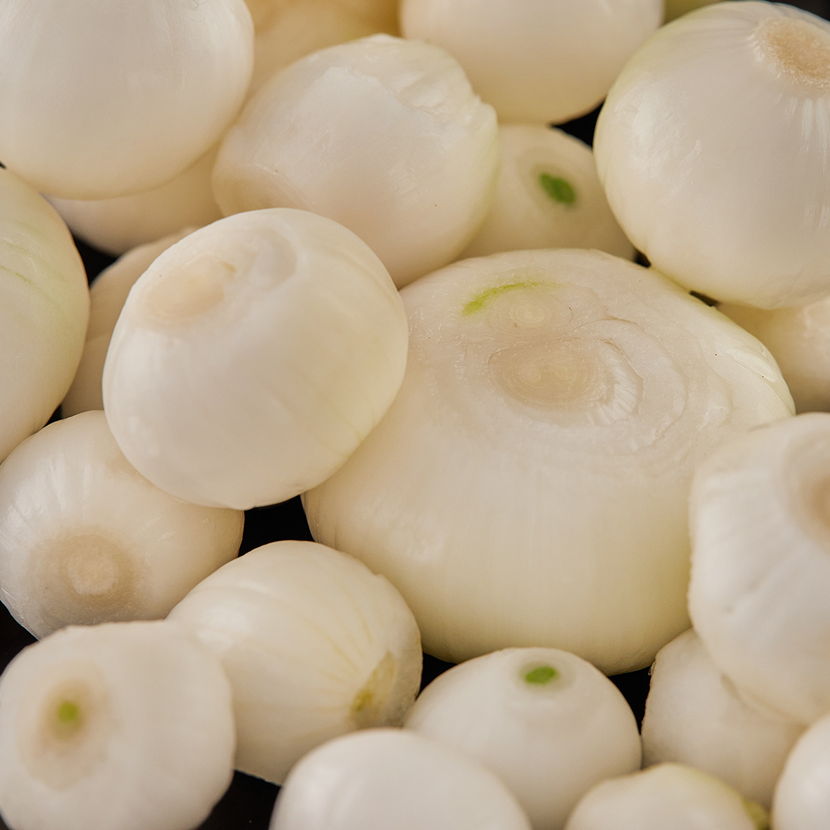 Shallots on black plate are peeled and ready to cook. Close up